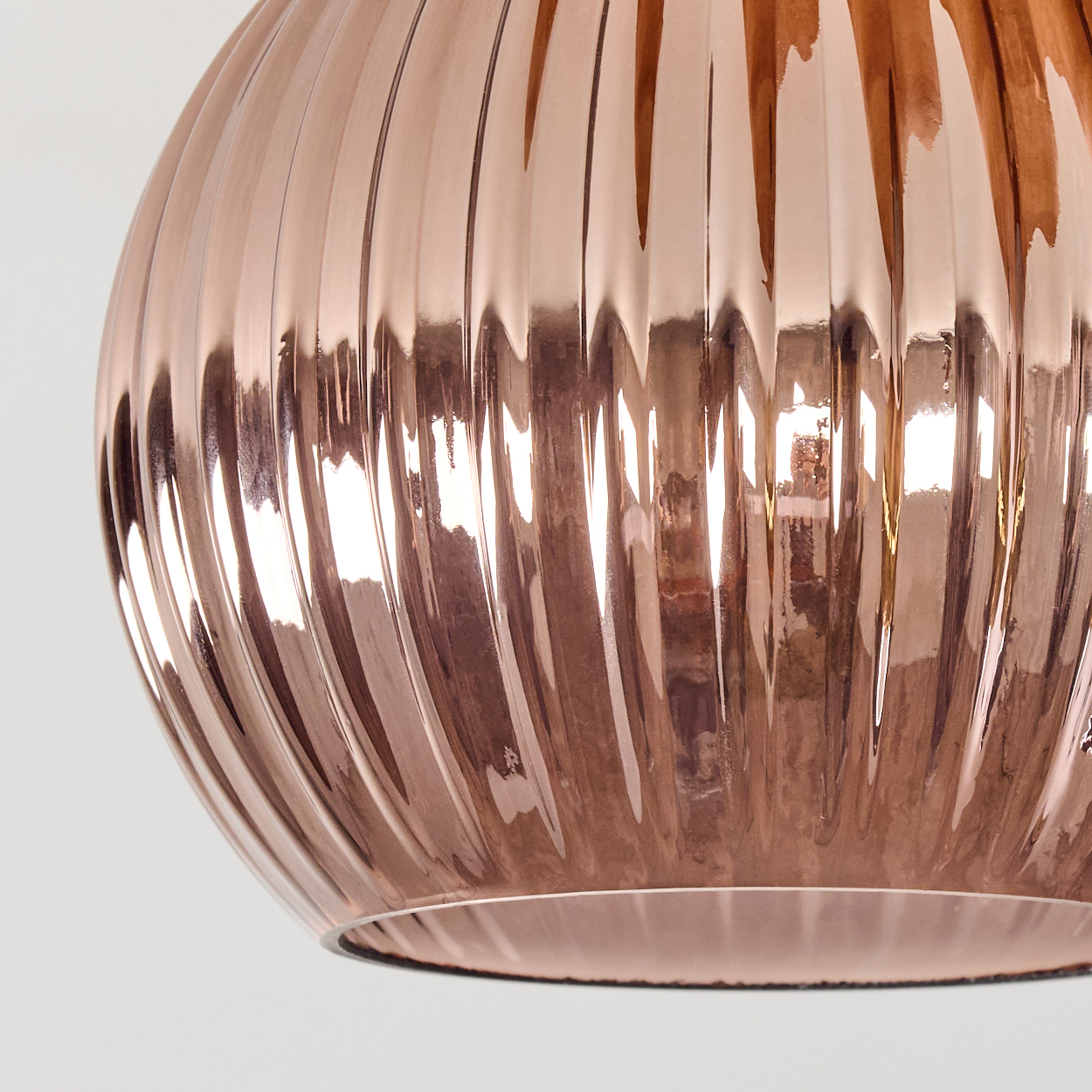 Nahaufnahme einer roségoldenen, gerippten Glaskugel vor weißem Hintergrund. Licht reflektiert auf der Oberfläche und erzeugt Glanzlichter.