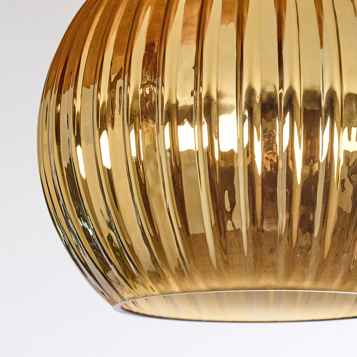 Nahaufnahme eines goldenen, gerippten Glaslampenschirms. Er reflektiert Licht und hat eine runde Form, vor weißem Hintergrund.