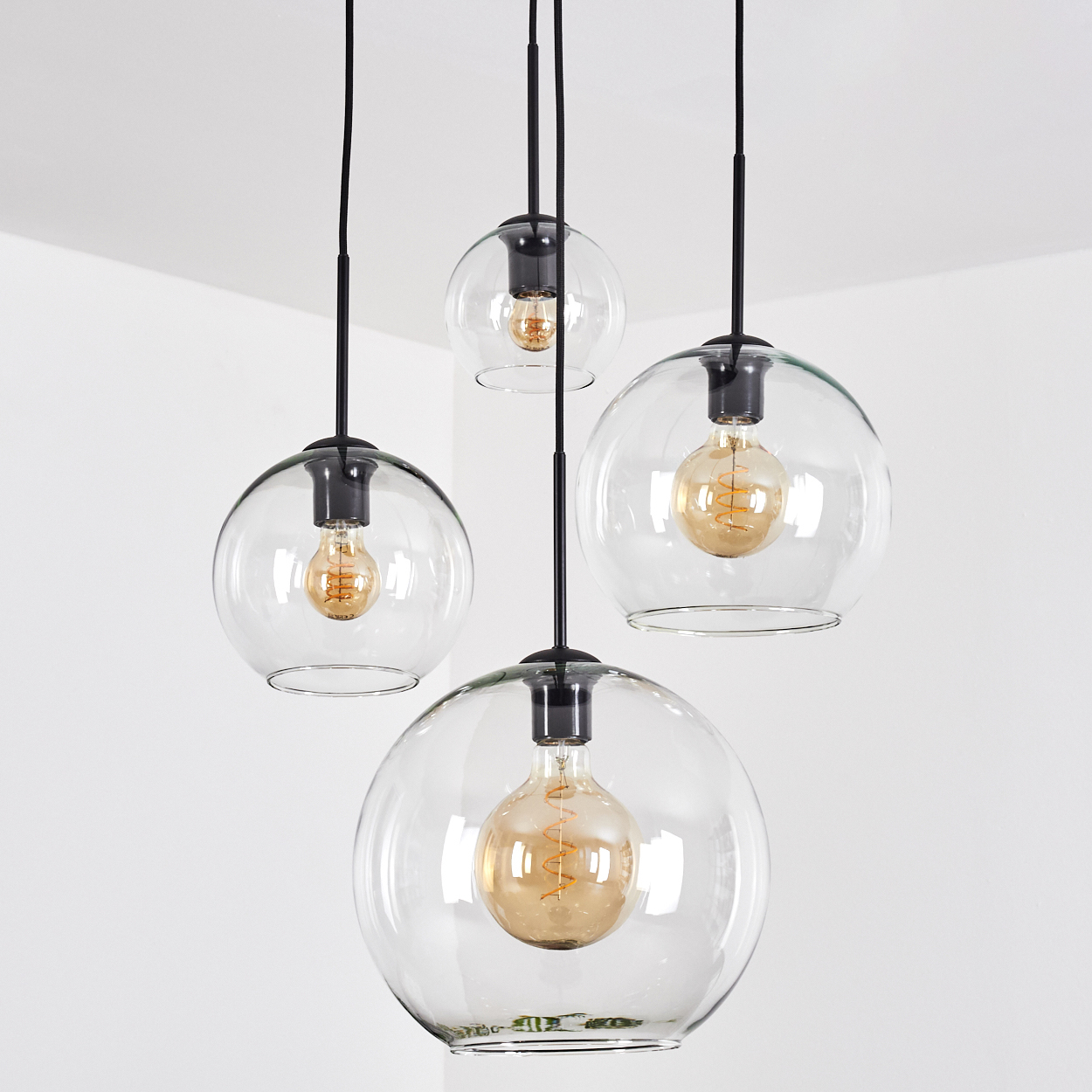 Vier Pendelleuchten mit Glaskugeln hängen von der Decke. Jede hat eine Glühbirne. Decke und Wände sind weiß.
