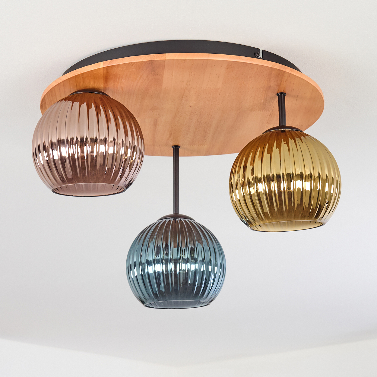 Eine Deckenleuchte mit drei Glaskugeln in Kupfer, Gold und Blau. Sie hängen an einer runden Basis aus Holz und Schwarz.