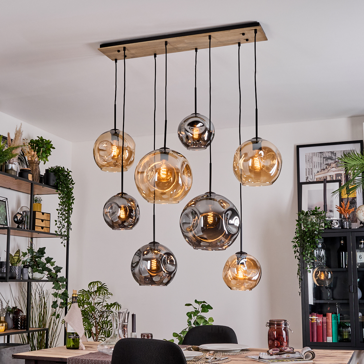 Ein Esszimmer mit Holztisch, schwarzen Stühlen und einer Leuchte mit kugelförmigen Lampen. Pflanzen und Dekoration sind ebenfalls sichtbar.