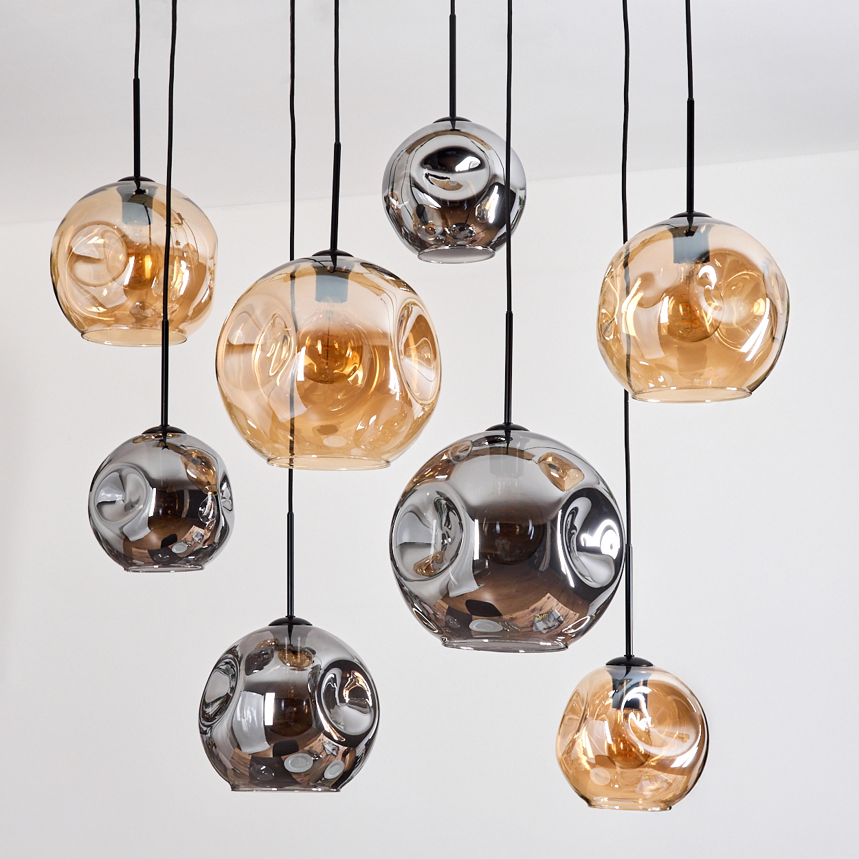 Mehrere Glas-Kugel-Pendelleuchten hängen von der Decke. Einige sind bernsteinfarben, andere verspiegelt silberfarben, alle mit schwarzen Kabeln.