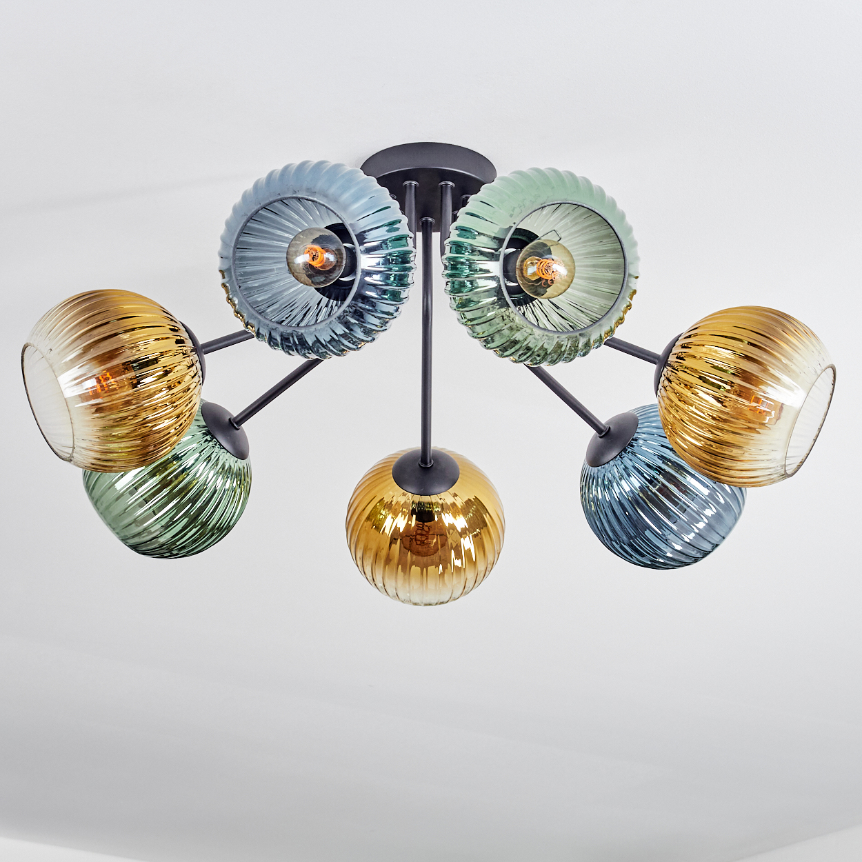 Eine moderne Deckenleuchte mit sechs Glasschirmen in verschiedenen Farben: Blau, Grün und Gold. Die Leuchte ist vor einer weißen Decke.