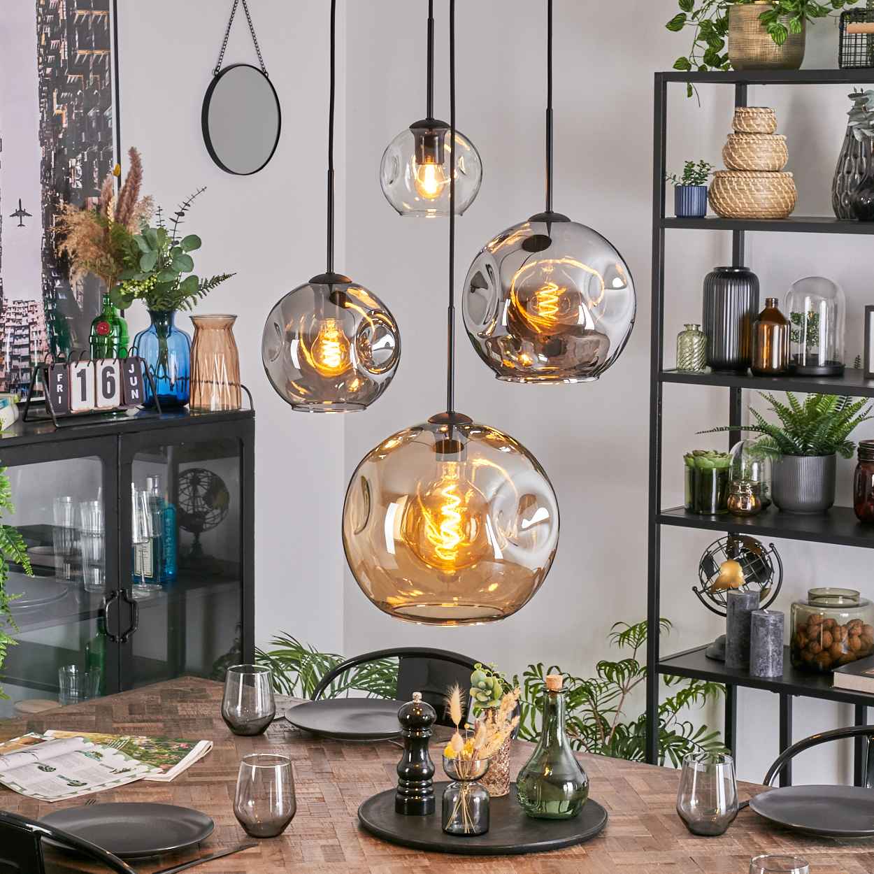 Esszimmer mit Hängelampen, gedecktem Tisch. Dekorative Gegenstände, Pflanzen und Regale im Hintergrund.