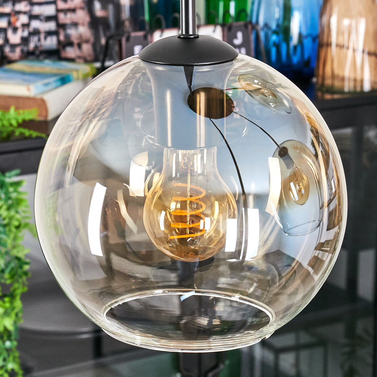 Eine klare Glaskugel-Leuchte mit einer warm getönten Glühbirne. Der Hintergrund hat verschwommene Objekte und Pflanzen.