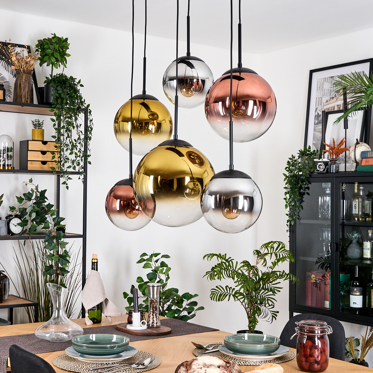 Esszimmer mit Pendelleuchten, gedecktem Tisch, Pflanzen und schwarzen Regalen mit Dekorationsartikeln.