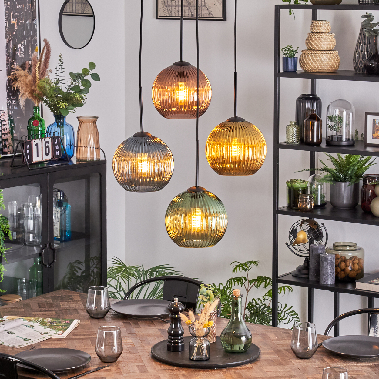Esszimmer mit Hängelampen, gedecktem Tisch und Regalen. Lampen sind Glaskugeln. Tisch hat Gläser und Teller. Regale haben Pflanzen.