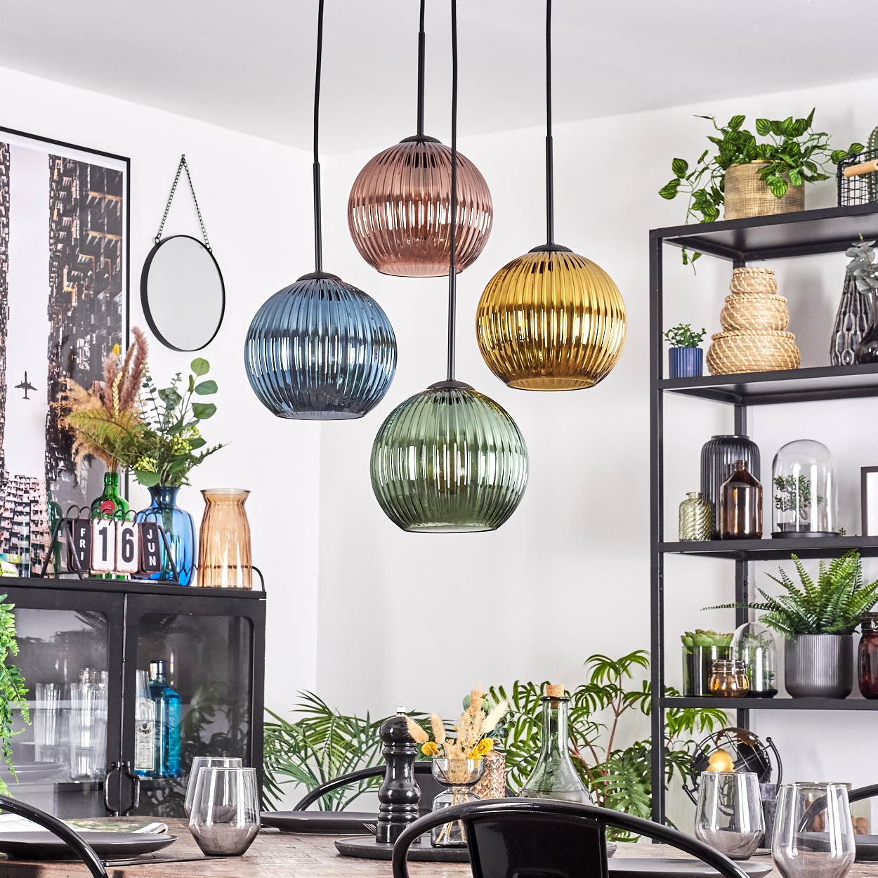 Esszimmer mit vier bunten Glas-Pendelleuchten. Ein schwarzer Schrank, ein Regal und Pflanzen sind sichtbar.