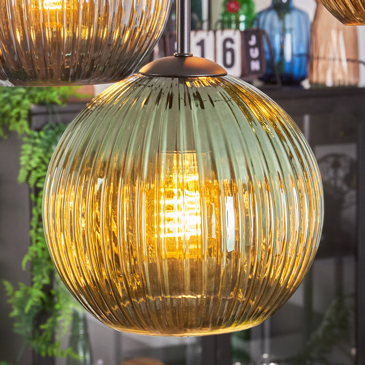 Nahaufnahme einer hängenden Glaslampe mit einer warmen Glühbirne im Inneren. Die Lampe ist eine Kugel mit vertikalen Rippen. Andere Lampen sind im Hintergrund.