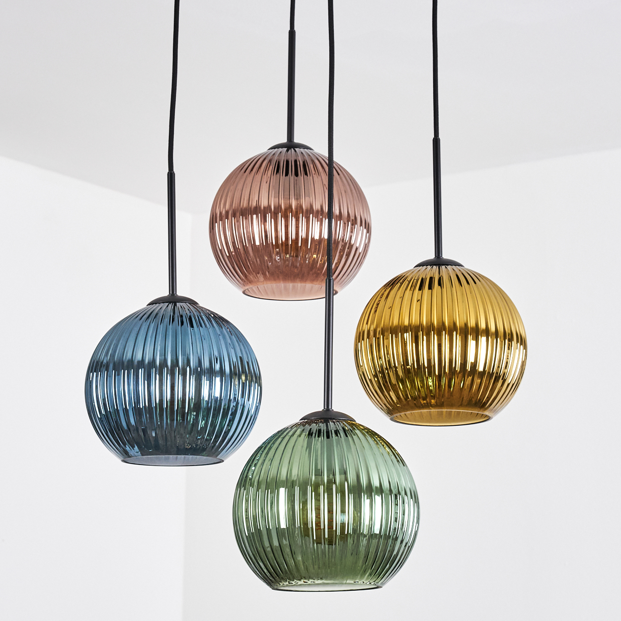 Vier bunte, gerippte Glas-Pendelleuchten hängen an schwarzen Kabeln. Farben sind blau, kupfer, gold und grün. Weißer Hintergrund.