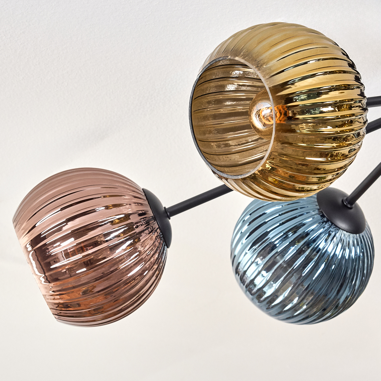 Eine moderne Deckenleuchte mit drei Glaskugeln in Gold, Kupfer und Blau vor weißem Hintergrund.