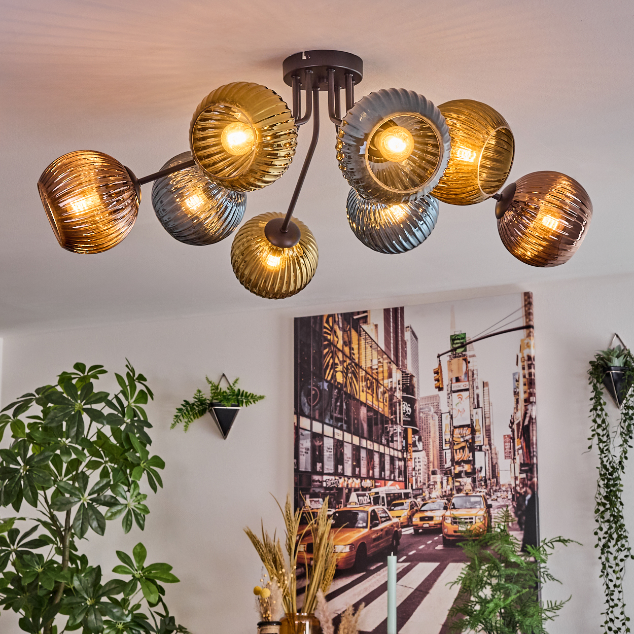 Eine moderne Deckenlampe mit Glaskugeln. Ein Gemälde einer Stadtszene an der Wand. Pflanzen im Vorder- und Hintergrund.