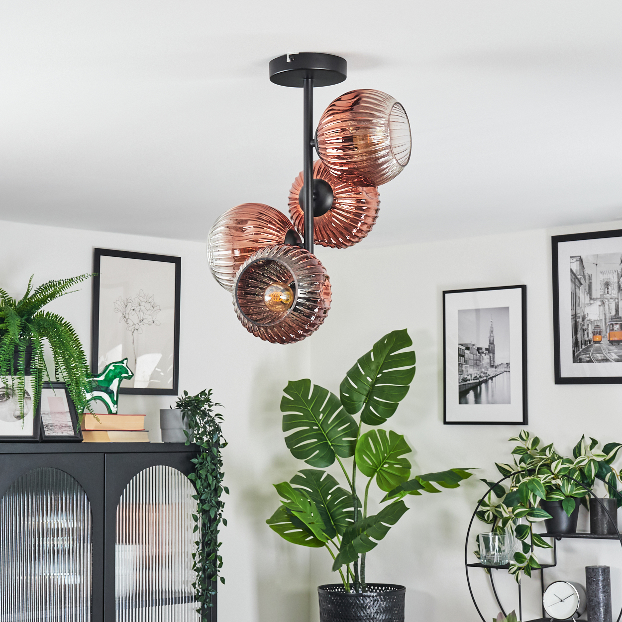 Ein modernes Wohnzimmer mit einem einzigartigen Kronleuchter, Pflanzen und gerahmten Bildern. Der Kronleuchter hat Glaskugeln. Verschiedene Pflanzen.