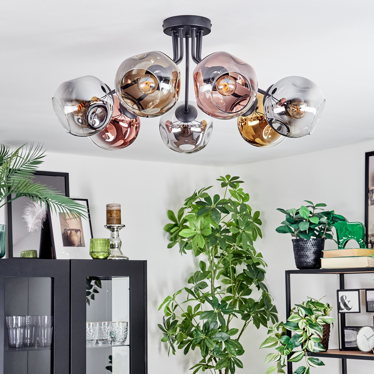 Eine moderne Deckenleuchte mit sechs Glaskugeln hängt von der Decke. Pflanzen und Möbel dekorieren den Raum. Verschiedene Dekorationsartikel sind sichtbar.