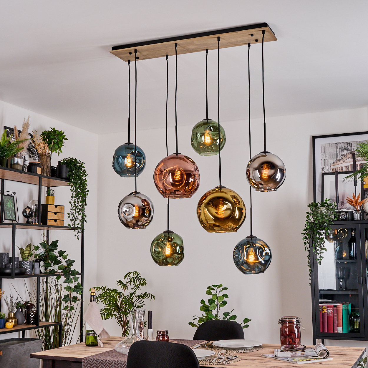 Esszimmer mit Holztisch und Kronleuchter mit bunten Glaskugeln. Regale und Pflanzen befinden sich auf beiden Seiten.