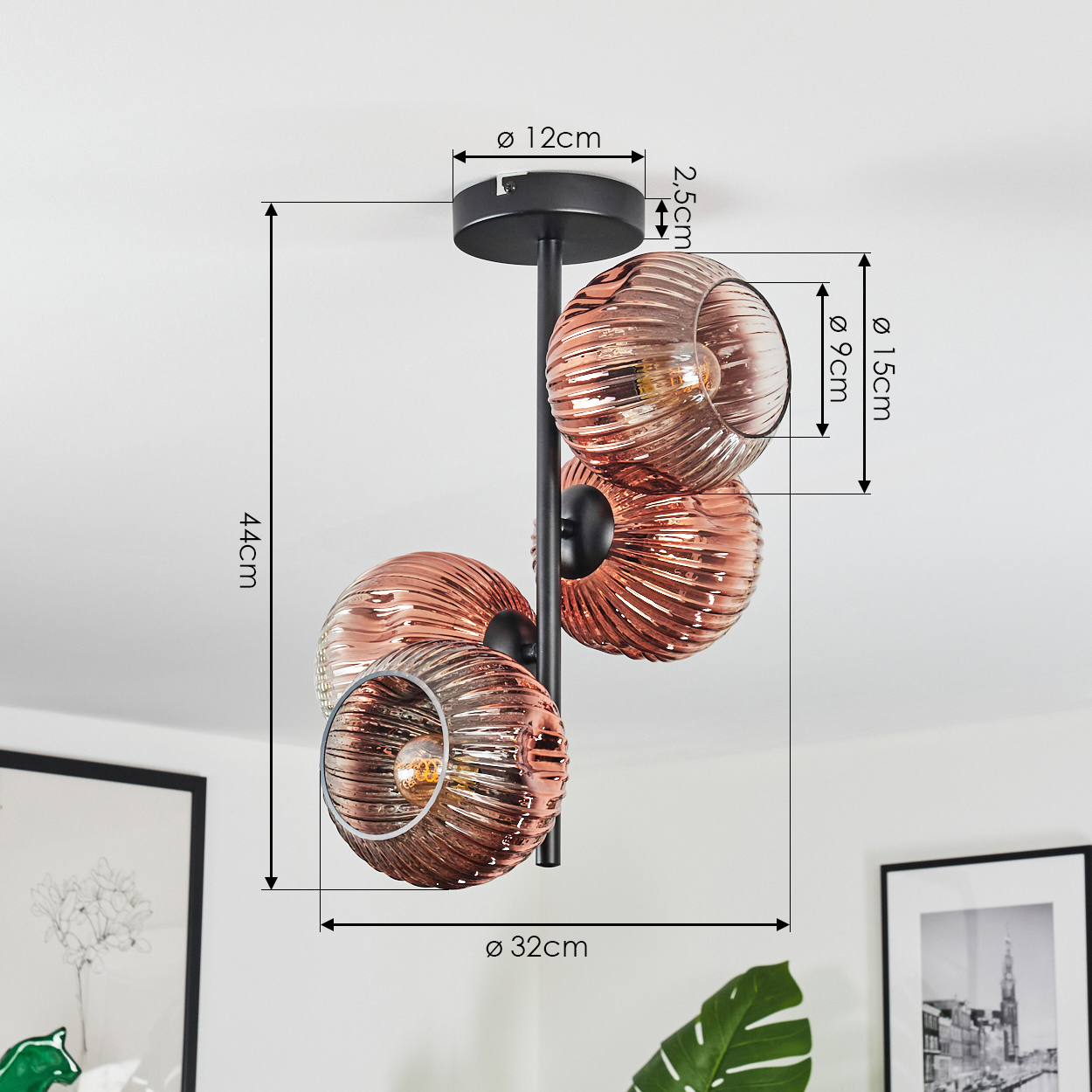Eine moderne Deckenlampe mit drei kugelförmigen, rosa getönten Glasschirmen. Die Lampe ist auf einem schwarzen Metallrahmen montiert.
