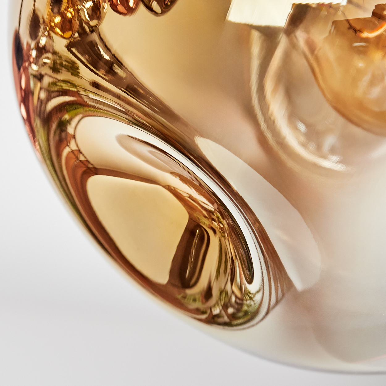 Nahaufnahme eines goldenen Glasobjekts, das Licht reflektiert. Die Oberfläche verformt die Reflexionen abstrakt.