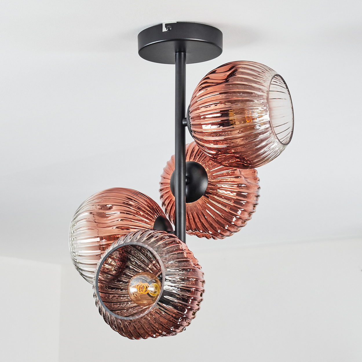 Moderne Deckenleuchte mit vier kupferfarbenen Glasschirmen. Schwarze Metallarme und Deckenhalterung. Weißer Deckenhintergrund.