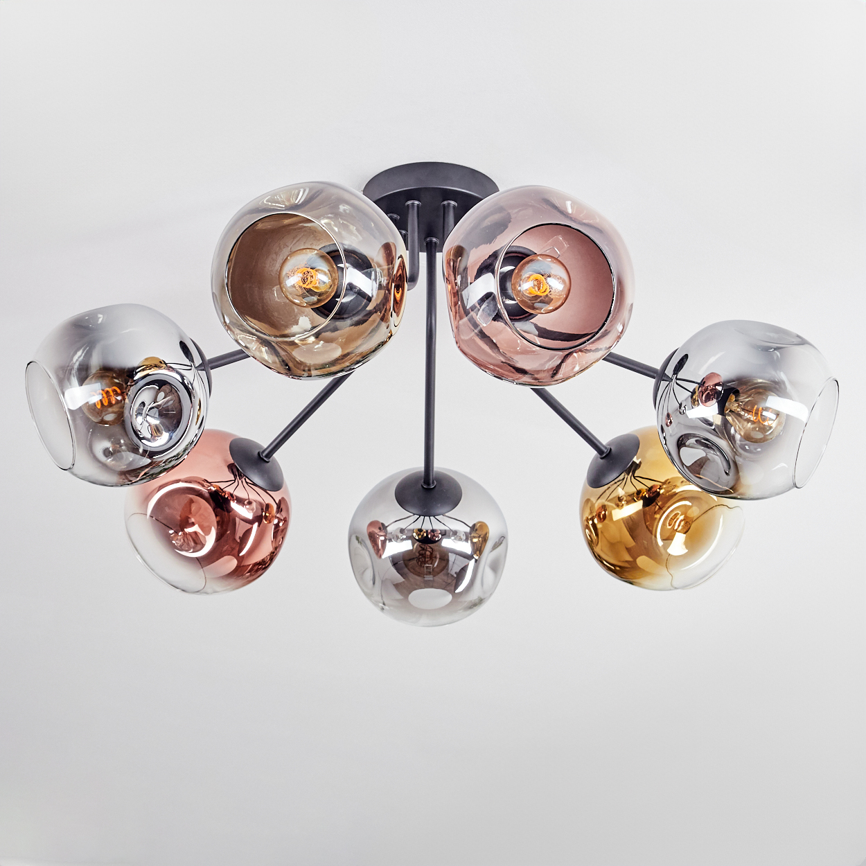 Eine moderne Deckenleuchte mit sieben Glaskugeln in verschiedenen Farben (Silber, Kupfer, Gold) und schwarzen Metallarmen, vor weißer Decke.