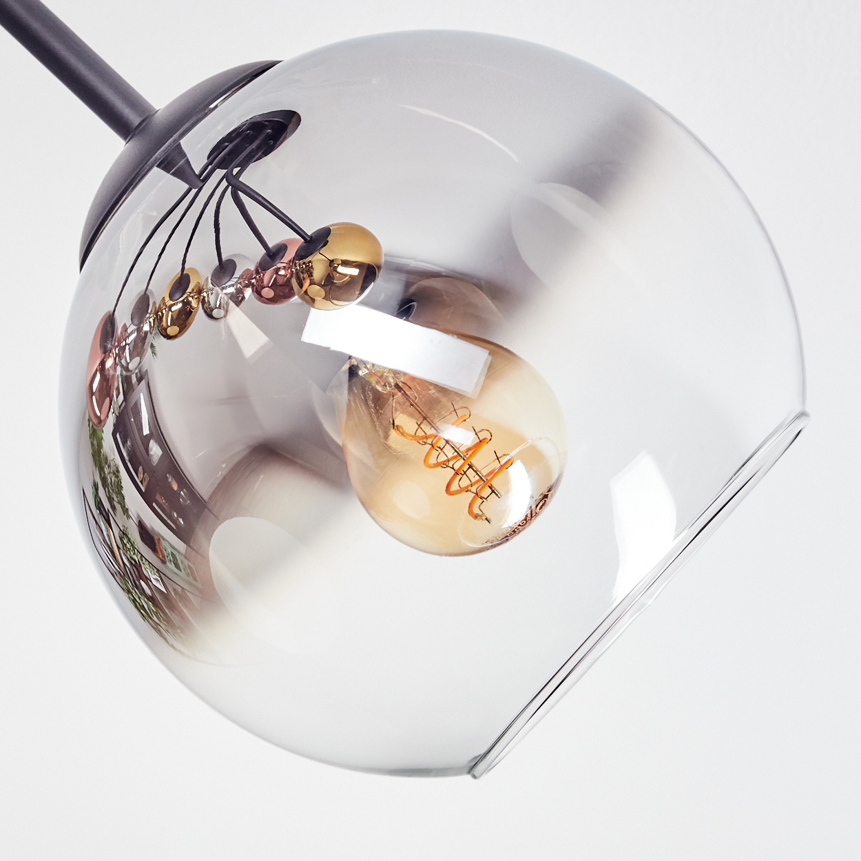 Eine moderne Pendelleuchte mit klarem, kugelförmigem Glasschirm. Im Inneren eine sichtbare Glühbirne. Dekorative Metallkugeln hängen darunter.
