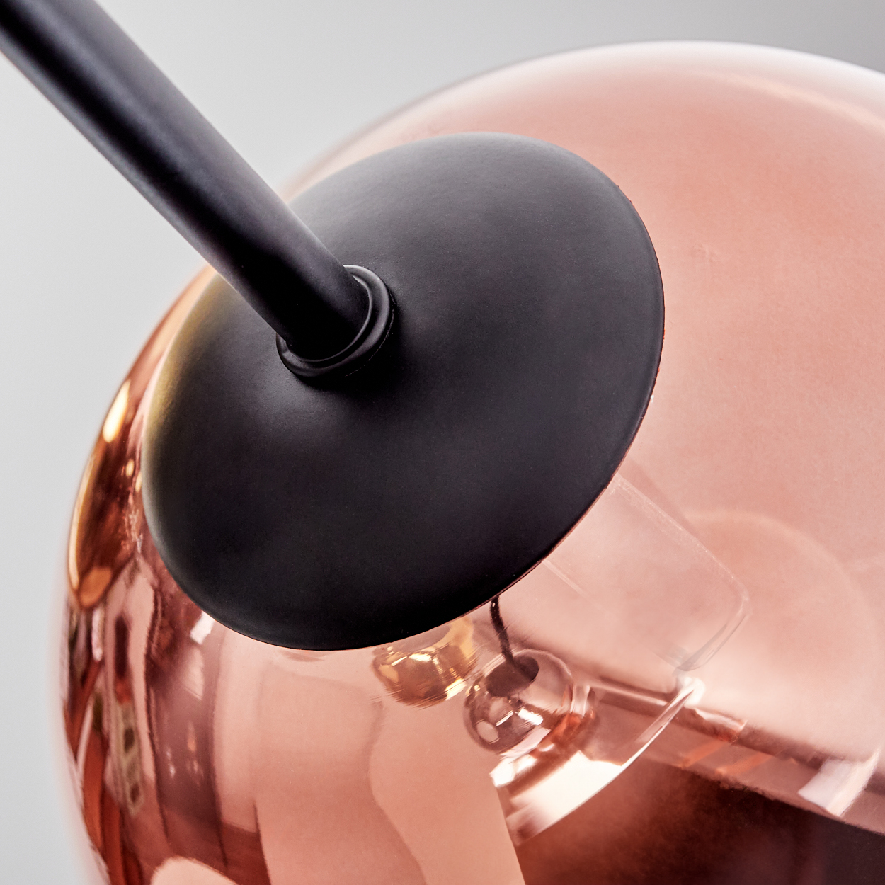 Nahaufnahme einer modernen Lampe. Sie hat einen schwarzen Arm und einen runden schwarzen Schirm. Die Glühbirne ist kupferfarben und reflektierend.