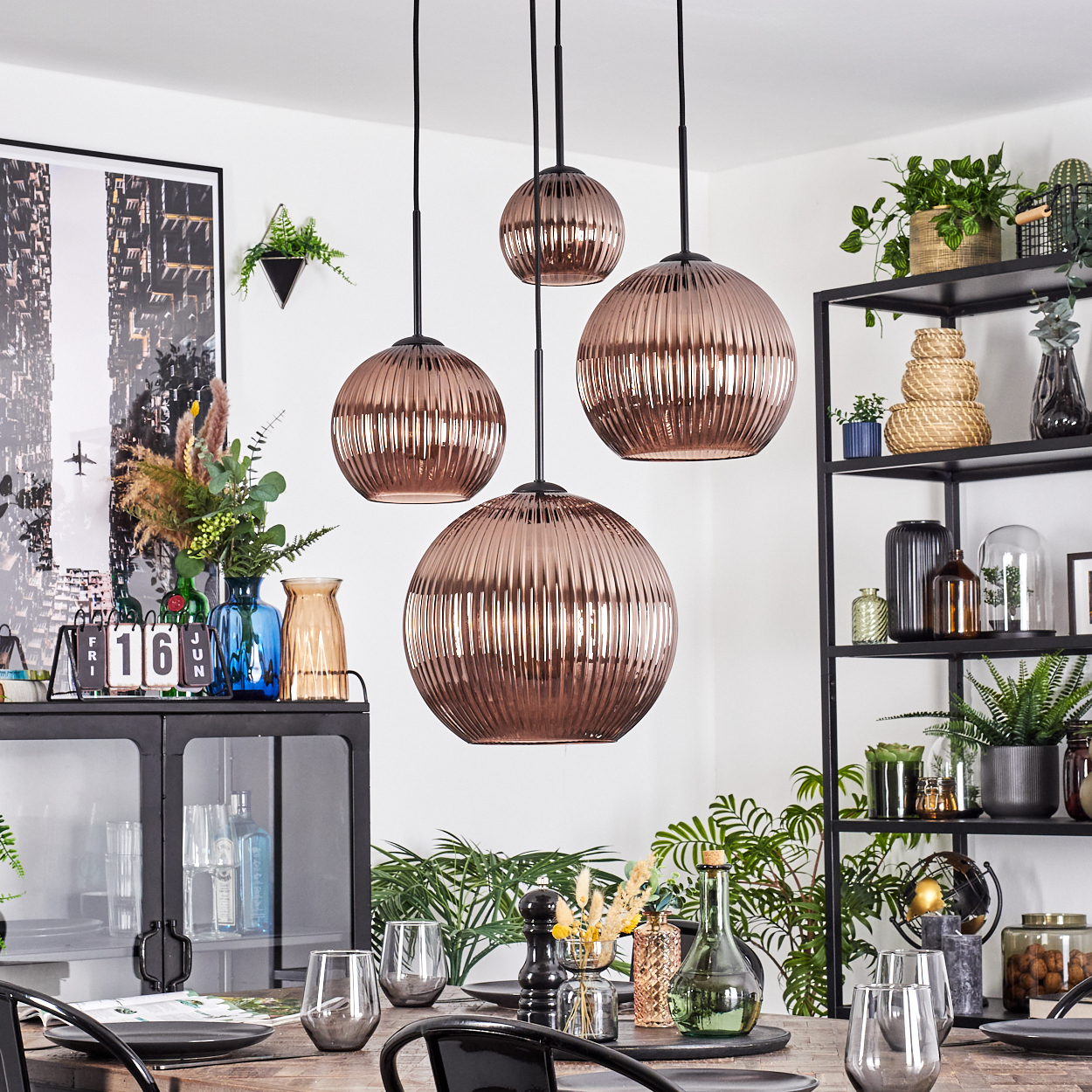 Esszimmer mit kupferfarbenen Pendelleuchten, Tisch mit Gläsern und einem schwarzen Schrank mit Pflanzen.