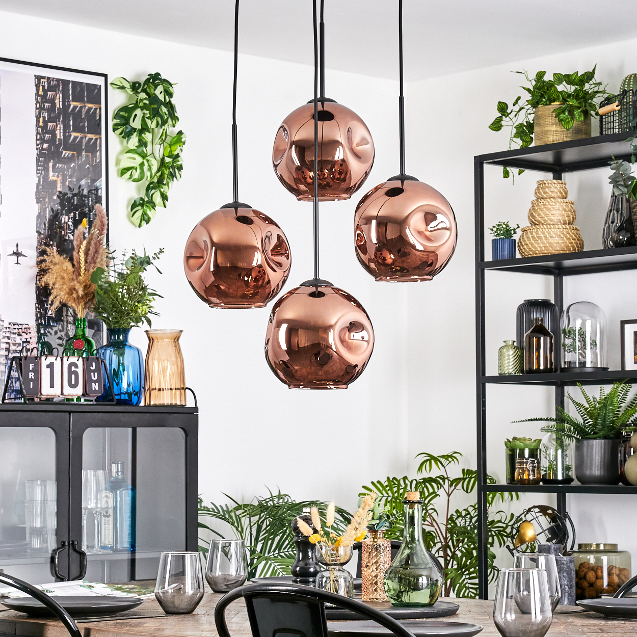 Esszimmer mit kupferfarbenen Pendelleuchten, gedecktem Tisch, Regalen mit Pflanzen und diversen Dekorationsartikeln.