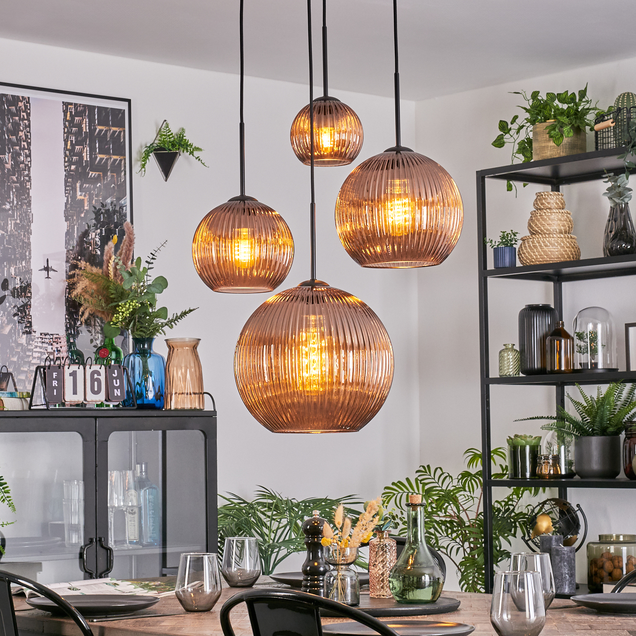 Esszimmer mit Kupfer-Pendelleuchten, Tisch mit Gläsern und Tellern sowie Pflanzen auf Regalen.