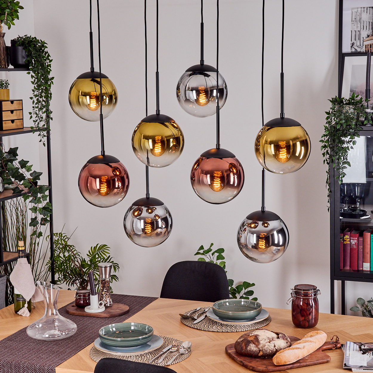 Esszimmer mit Pendelleuchten. Tisch gedeckt mit Tellern, Brot und Glas. Kugelförmige Lampen in verschiedenen Farben hängen.
