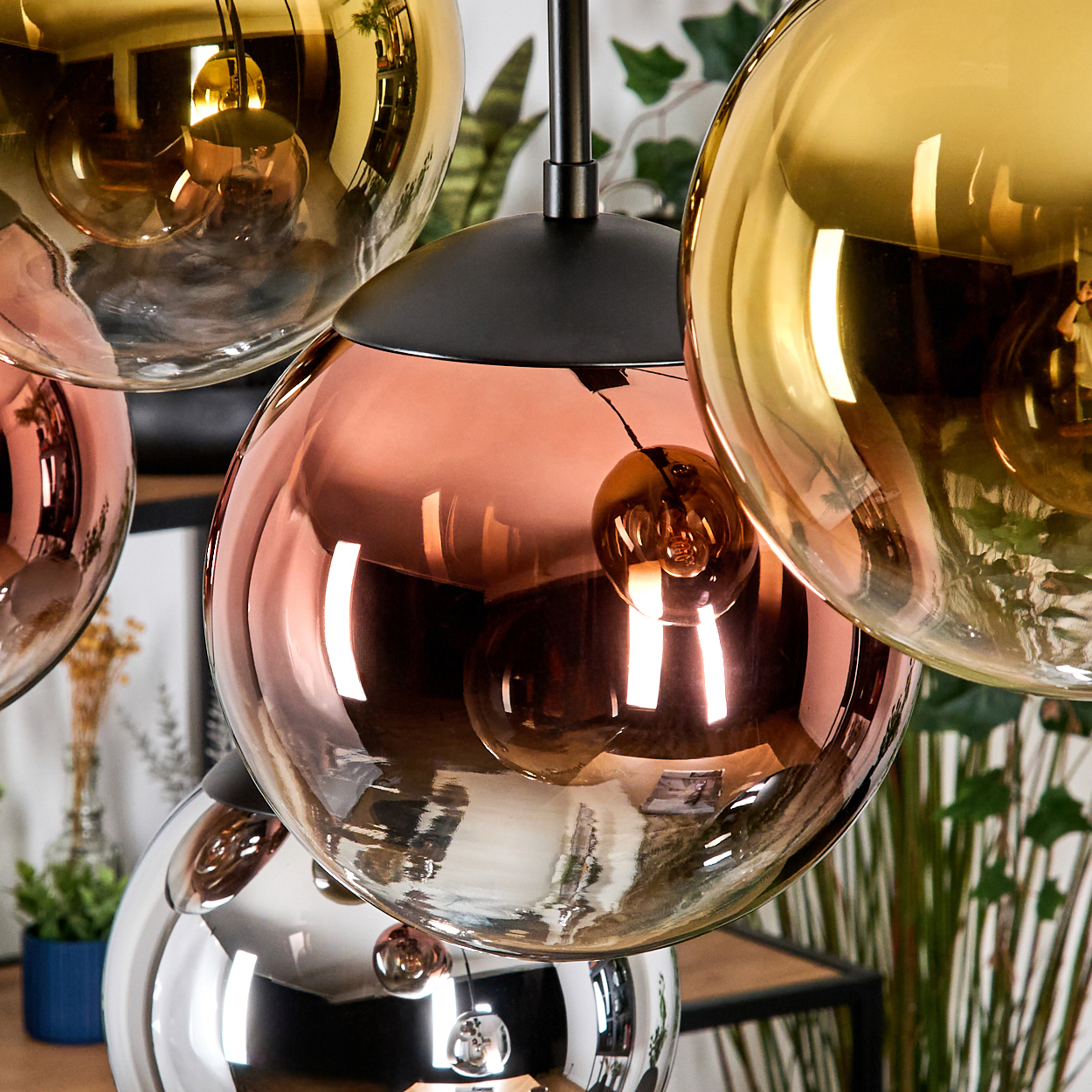 Nahaufnahme eines modernen Kronleuchters mit mehreren kugelförmigen Glasschirmen in Kupfer-, Gold- und Silberfarben. Die Glühbirnen sind sichtbar.