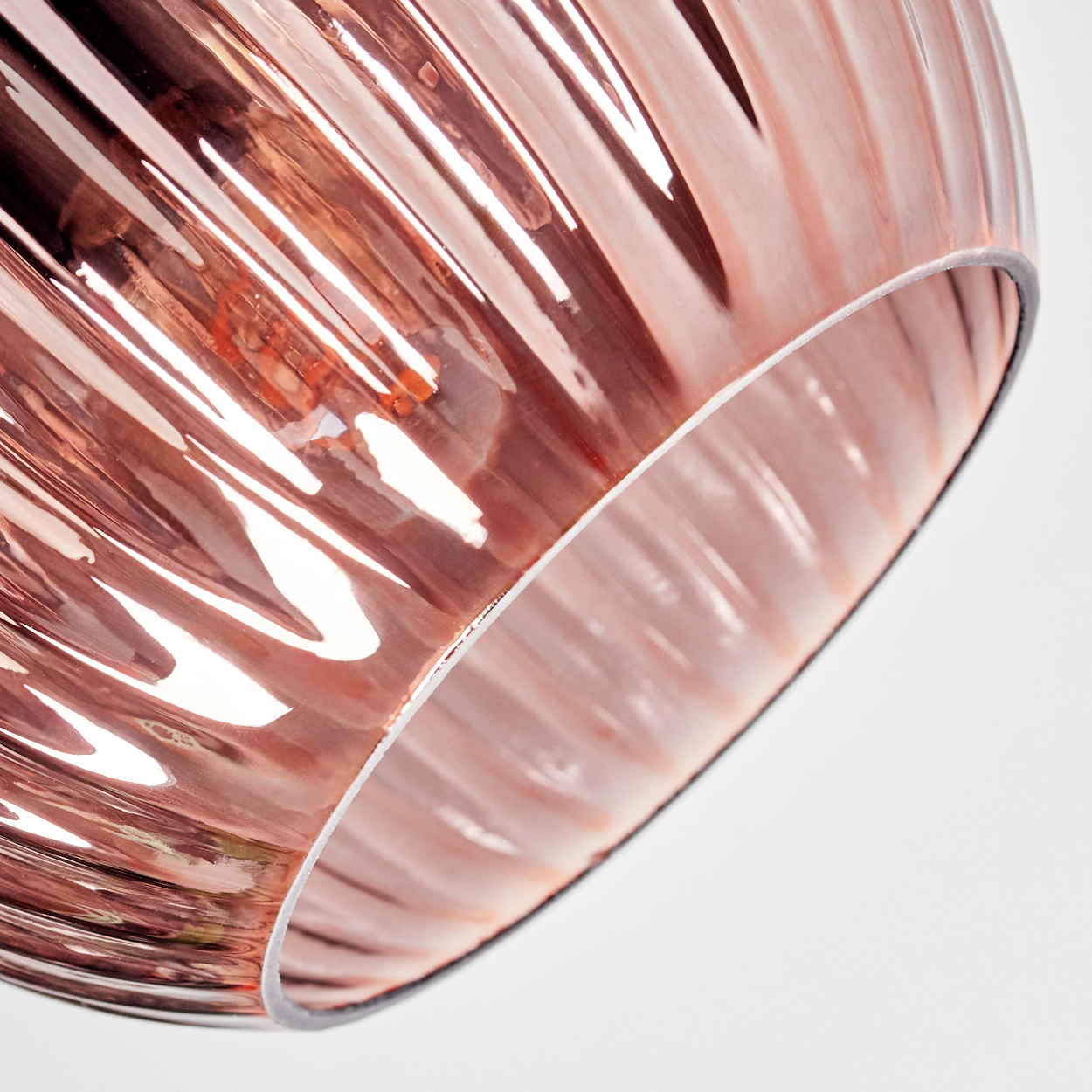 Nahaufnahme eines roségoldenen, gerippten Glasschirmes vor weißem Hintergrund. Die Glühbirne ist im Inneren zu sehen.