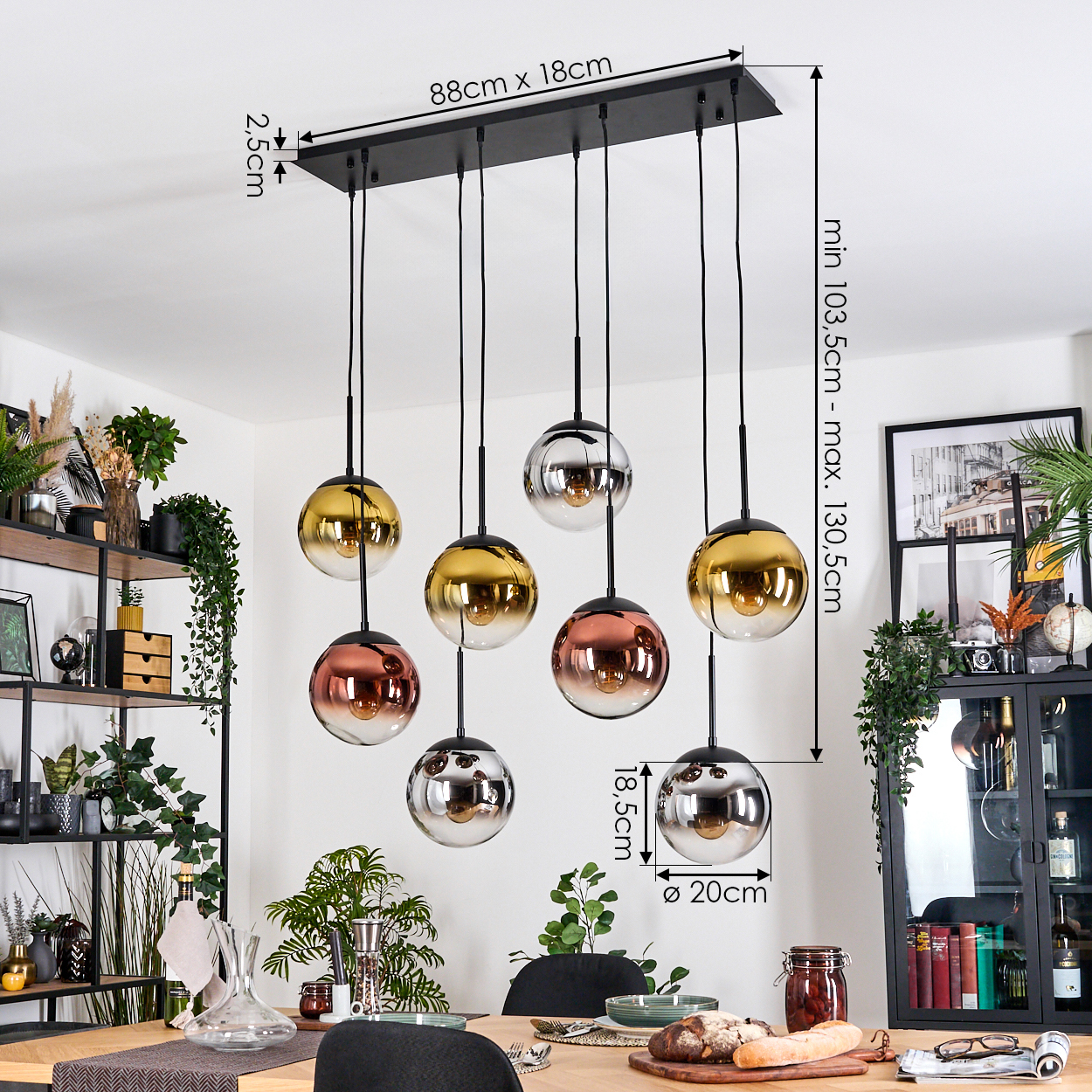 Ein modernes Esszimmer mit einem schwarzen Kronleuchter mit Glaskugeln in verschiedenen Farben. Der Tisch ist mit Essen und Pflanzen gedeckt.