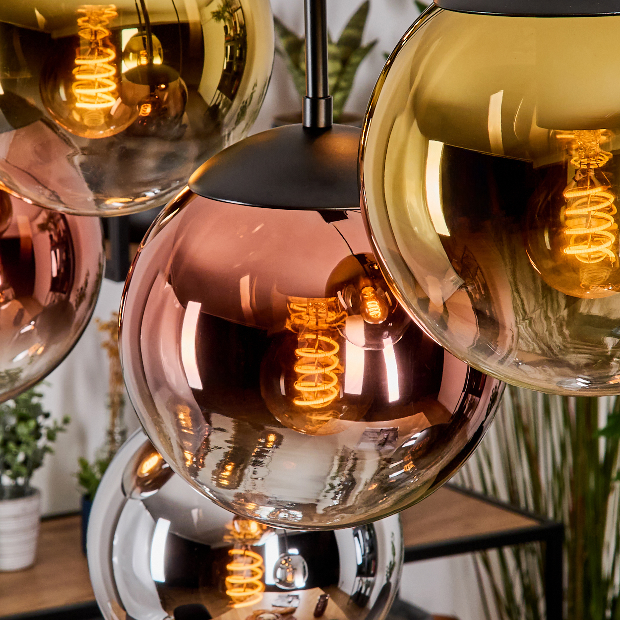 Nahaufnahme eines modernen Kronleuchters mit mehreren kugelförmigen Glasschirmen in Kupfer, Gold und Silber, jede mit einer sichtbaren Glühbirne.