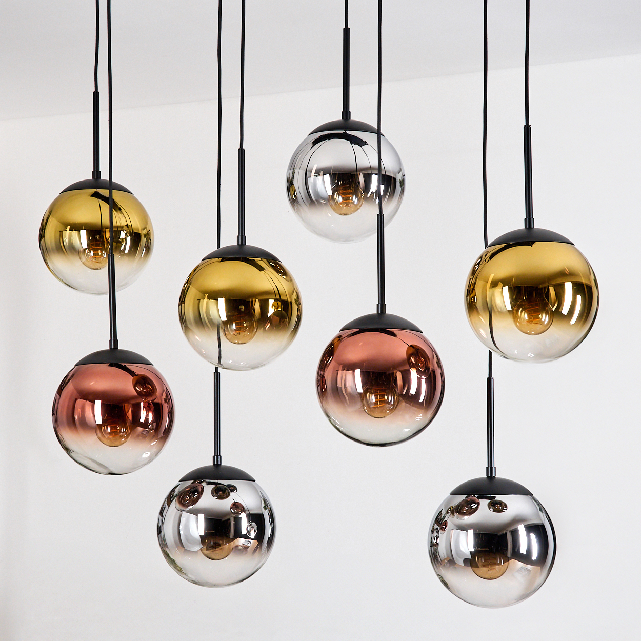Acht kugelförmige Pendelleuchten mit farbigen Glasschirmen. Gold-, Silber- und Kupfertöne hängen vor weißem Hintergrund.