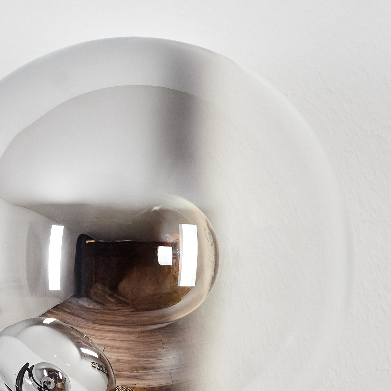 Nahaufnahme einer silbernen, kugelförmigen Lampe vor einer weißen Wand. Reflexionen sind auf der Oberfläche zu sehen.