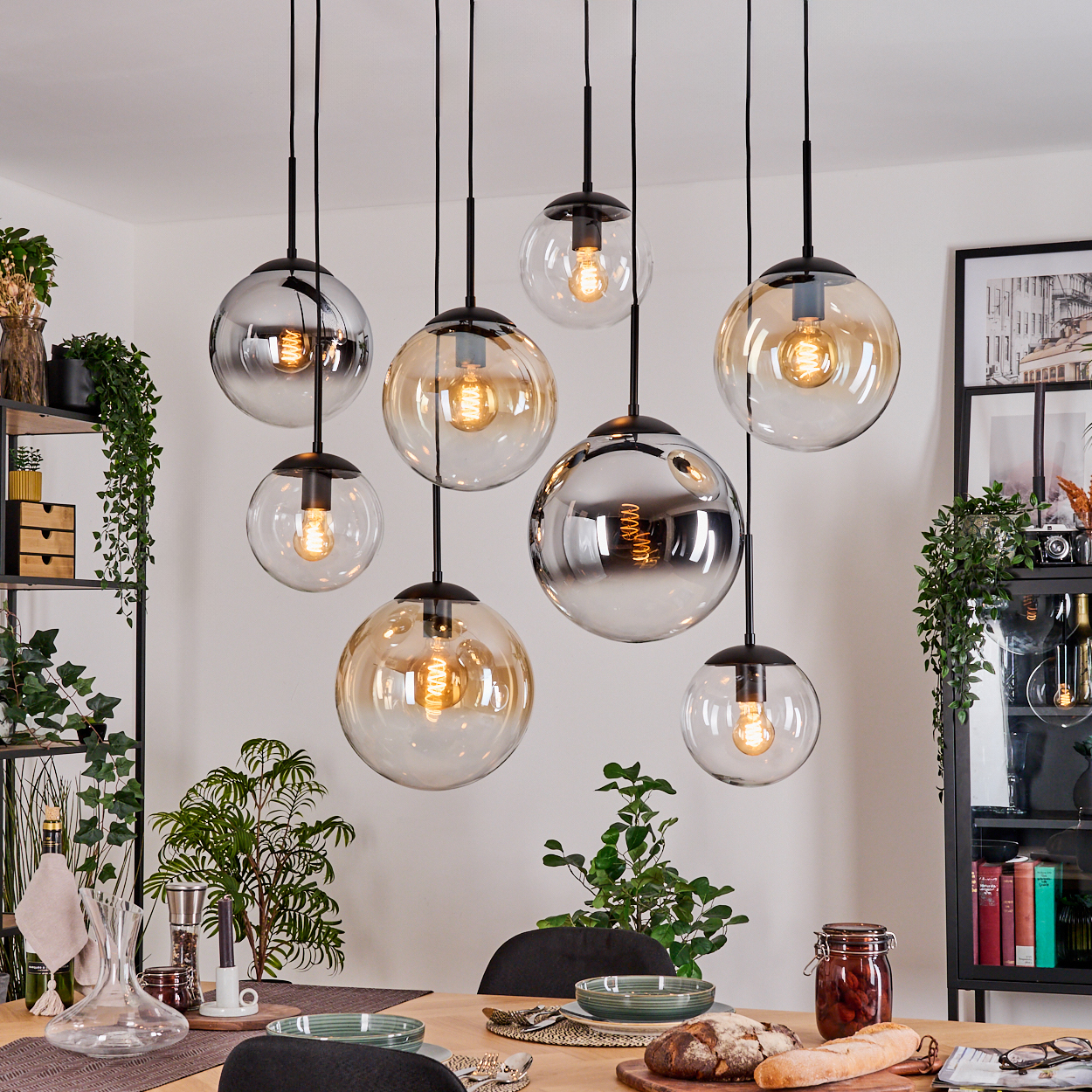 Esszimmer mit hängenden Kugelleuchten. Tisch mit Pflanzen und Essen gedeckt. Regale mit Gegenständen im Hintergrund.
