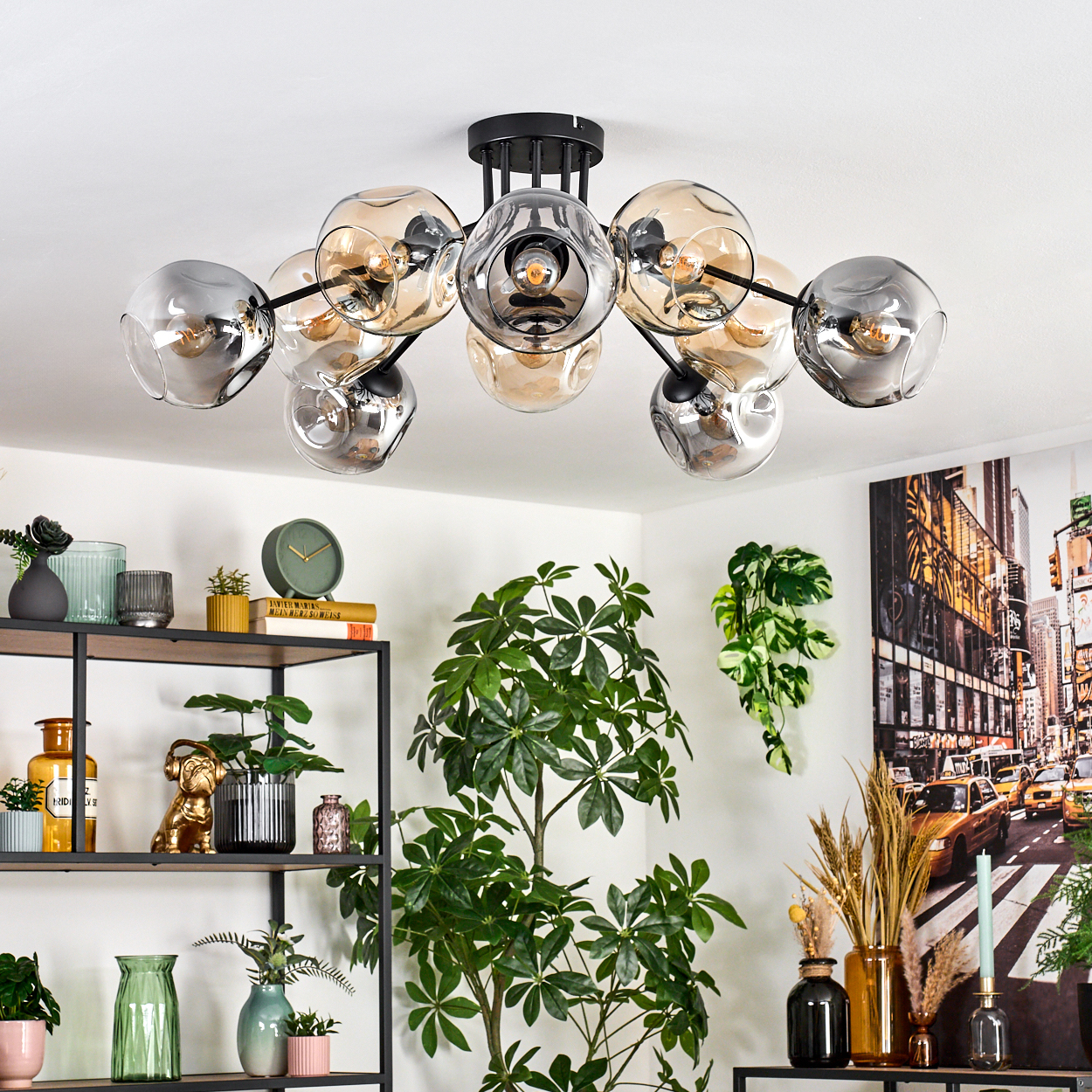 Eine moderne Deckenleuchte mit Glaskugeln hängt von der Decke. Regale zeigen Pflanzen und Dekor, mit einem Stadtbildgemälde an der Wand.