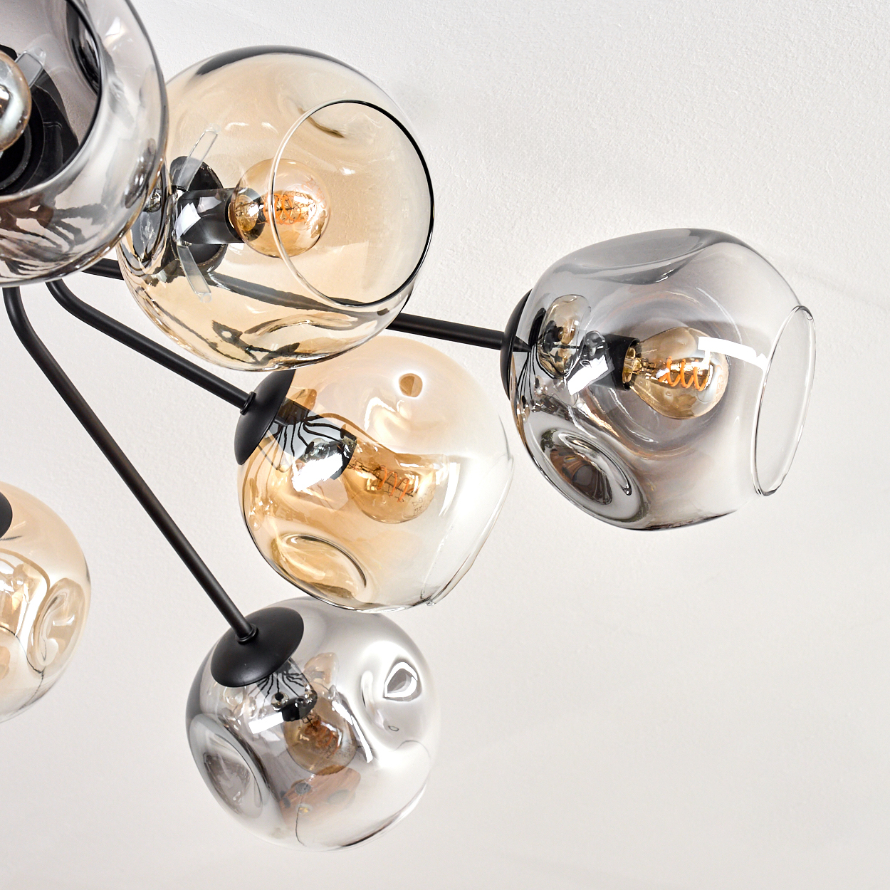 Moderner Kronleuchter mit mehreren kugelförmigen Glasschirmen in Bernstein und Grau, jede mit einer Glühbirne. Schwarze Metallarme auf weißem Hintergrund.