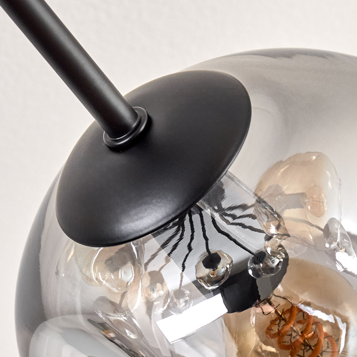 Nahaufnahme einer modernen Lampe. Ein schwarzer Metallarm und eine Scheibe tragen einen rauchigen Glaskolben mit Glühbirne.