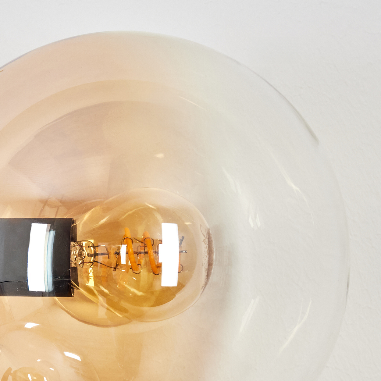 Nahaufnahme einer Glühbirne in einer Glaskugel. Die Glühbirne leuchtet orange, die Kugel hat einen Farbverlauf von Bernstein zu klar.