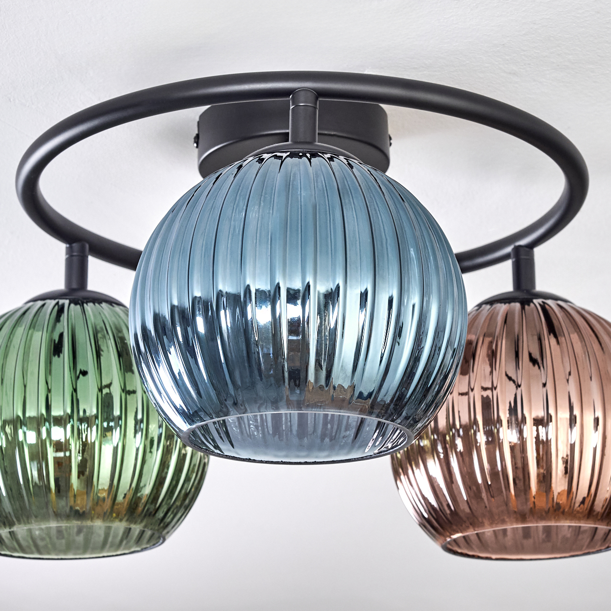 Eine moderne Deckenleuchte mit drei Glaskugeln in Grün, Blau und Kupferfarben, befestigt an einem schwarzen Metallrahmen.