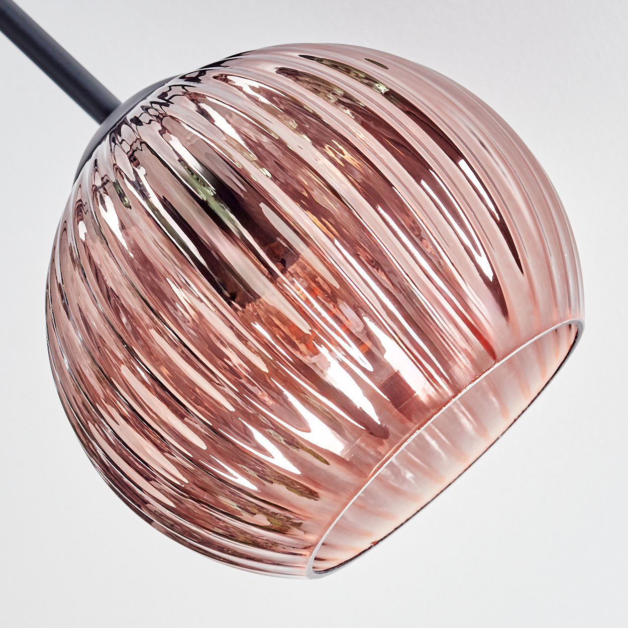 Ein roségoldener, gerippter Glasschirm hängt an einem schwarzen Arm. Das Licht reflektiert sich im Glas. Der Hintergrund ist weiß.