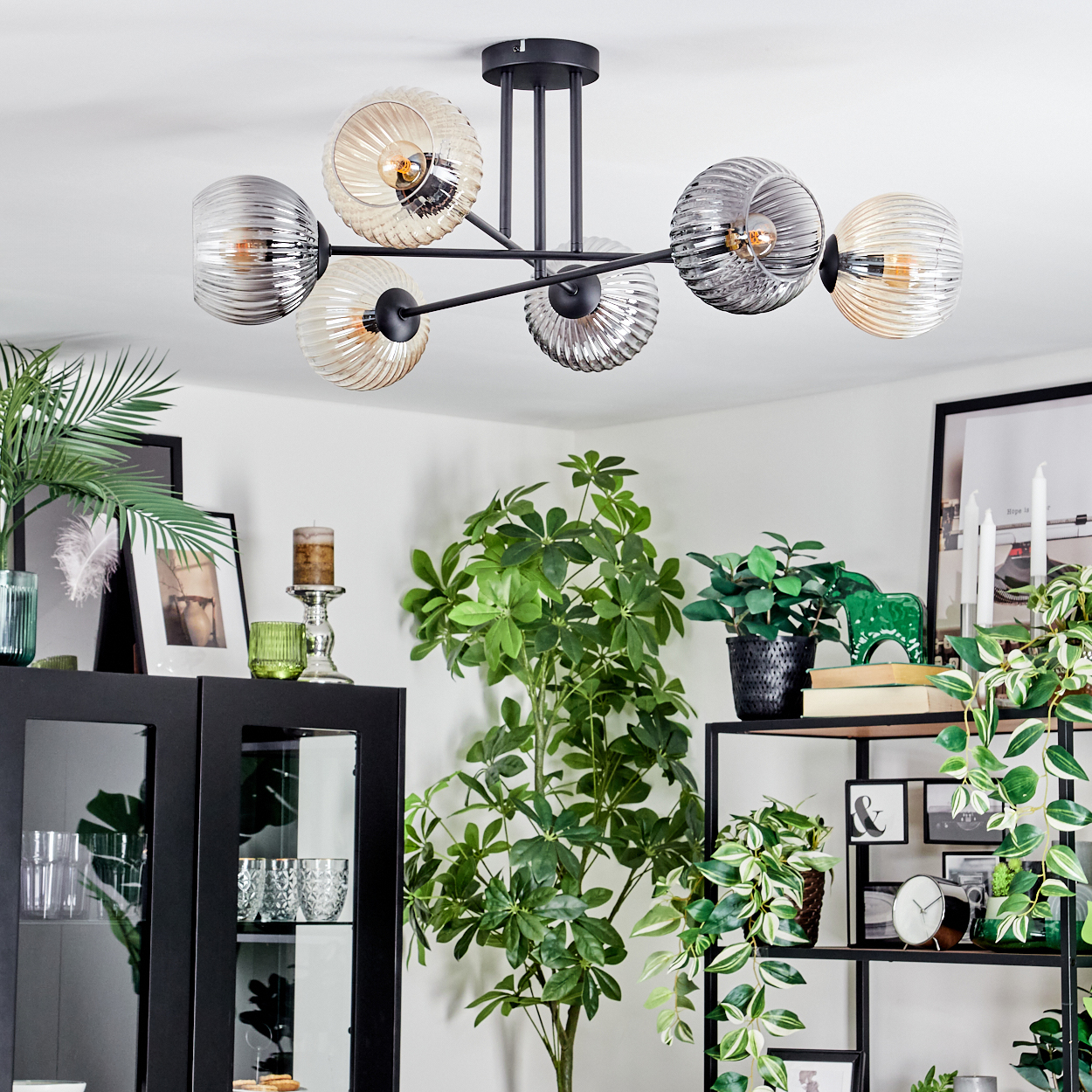 Ein modernes Wohnzimmer mit Kronleuchter, Pflanzen und Dekorationsartikeln. Schwarze Regale und Schrank. Grüne und weiße Pflanzen.