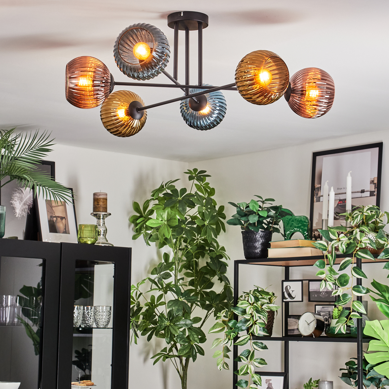 Eine moderne Deckenleuchte mit kugelförmigen Lampen, umgeben von Pflanzen und Möbeln in einem Wohnzimmer.