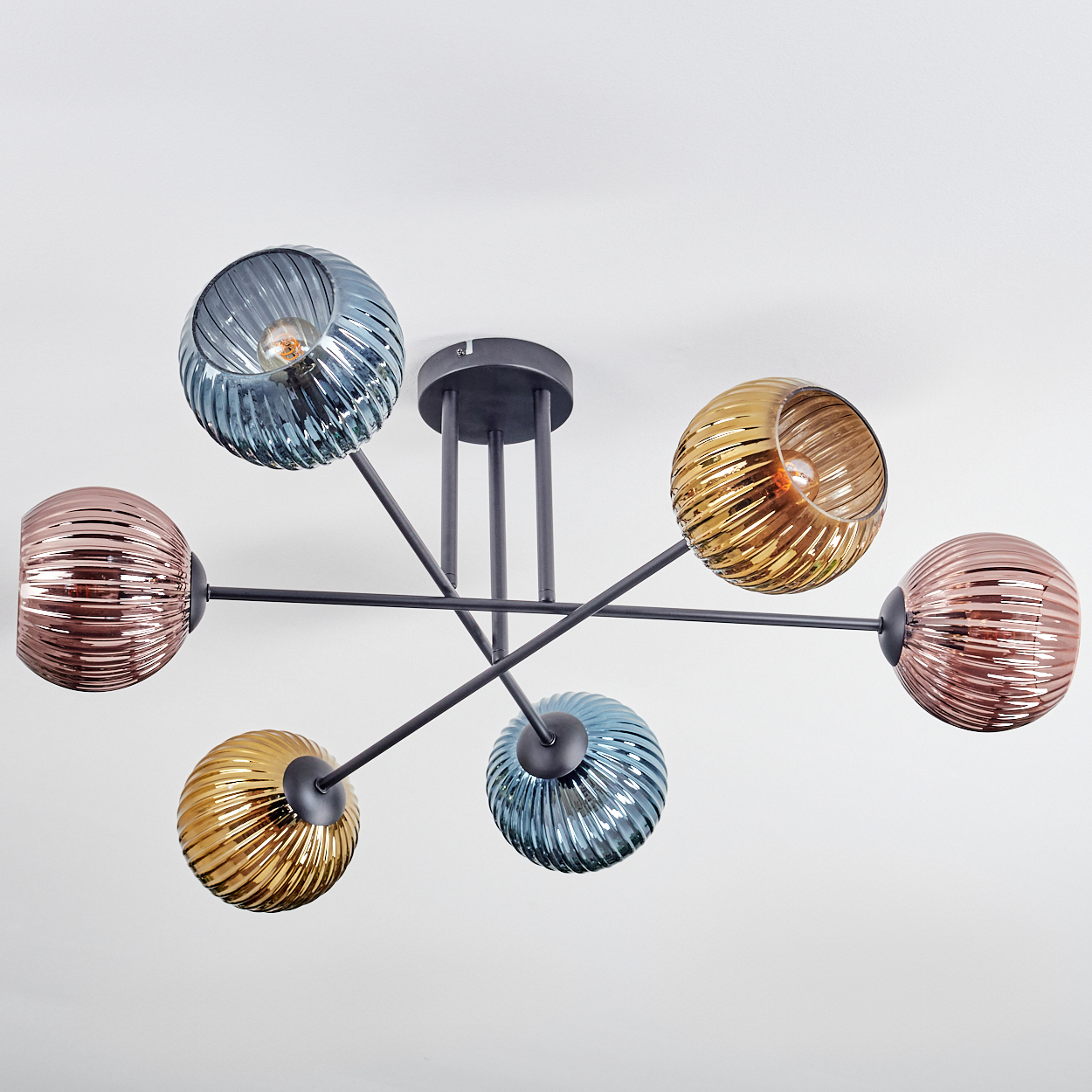Eine moderne Deckenleuchte mit sechs kugelförmigen, gerippten Glasschirmen in Blau, Gold und Rosa, an schwarzen Armen, vor weißem Hintergrund.