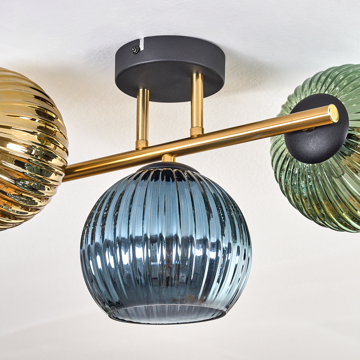 Deckenlampe mit drei Glasschirmen: Gold, Blau und Grün. Gold- und Grünschirme sind gerippt. Die Leuchte hat einen schwarzen Sockel und goldene Arme.