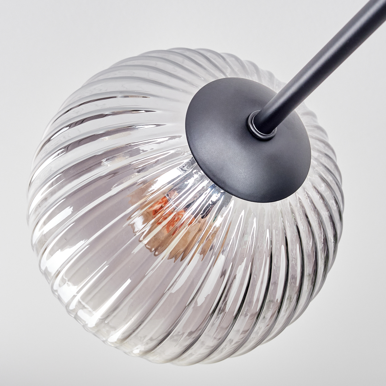 Nahaufnahme einer Glaslampe mit schwarzem Metallarm. Das Glas ist transparent mit Spiraldesign. Der Hintergrund ist weiß.