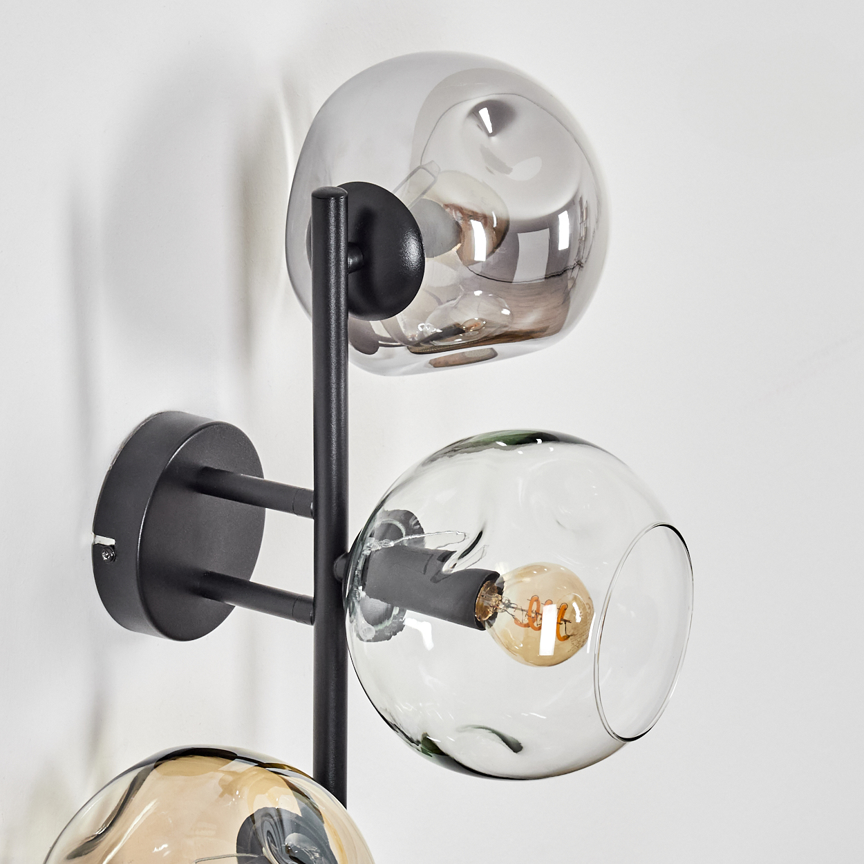 Eine moderne Wandlampe mit drei Glaskugeln. Die Lampe ist schwarz, die Kugeln sind transparent und die Wand ist weiß.