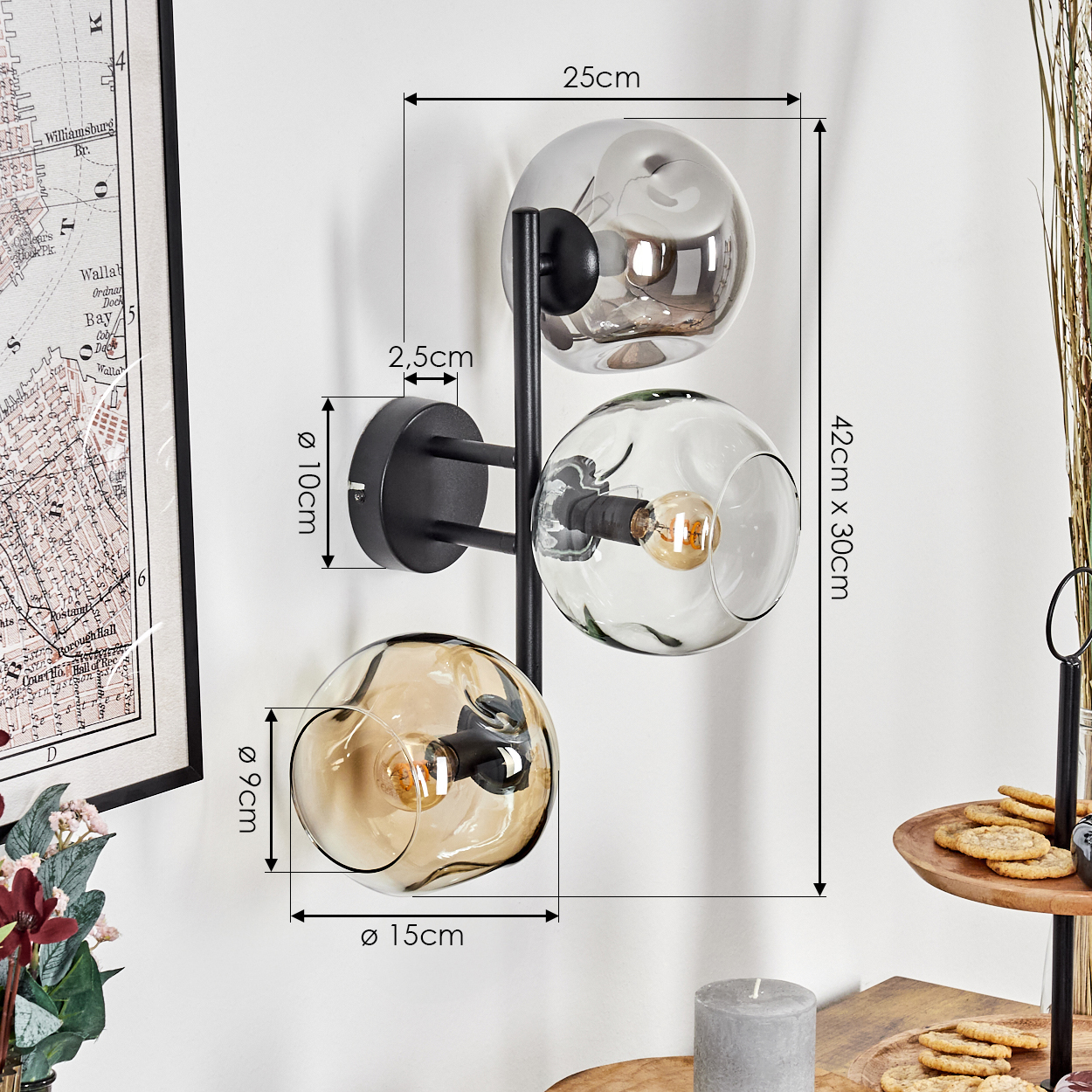Eine moderne Wandlampe mit drei Glaskugeln. Maße sind angegeben. Eine Karte und ein Tisch mit Snacks sind ebenfalls sichtbar.