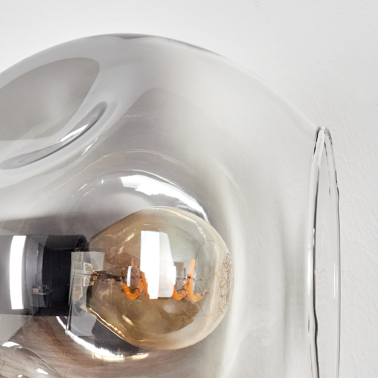 Nahaufnahme einer Leuchte mit klarem Glasschirm und sichtbarer Glühbirne. Die Glühbirne hat einen Spiralglühfaden und orangefarbene Details.